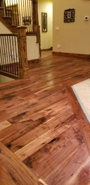 A dark, richly figured acacia floor in an entryway beside a wooden staircase